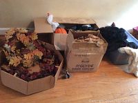 Box with autumn leaf wreaths, several cardboard boxes and containers with other decorations visible