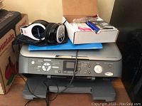 Wide view showing Epson Stylus CX7800 printer with Monoprice headphones and box of spare ink cartridges on top.