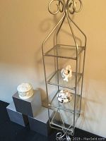 Photo showing metal wall shelf with scroll design, trinket boxes and cherub figurine on shelves, and three cubic wall blocks arranged nearby.