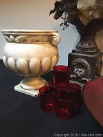 Photo of large cream-colored decorative urn, red bowl, and five red glass tumblers grouped together.
