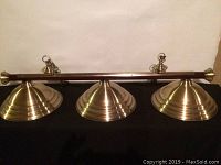 Front view of brass 3-light pool table fixture with three dome-shaped shades and mounting hooks.