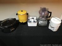 Four kitchen appliances shown: black Crock-Pot slow cooker, yellow coffee percolator, white Braun juicer, KitchenAid food processor