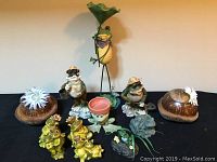 Front view of assortment with tall metal frog holding leaf at center, smaller frog figurines around it, and coconut shell containers on sides