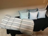 Two Muskoka chair cushions and six outdoor throw pillows arranged on a black cloth.