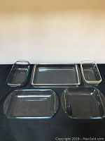 Top down view of five assorted clear glass bakeware dishes placed side by side on a black surface.