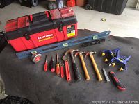 Photo showing Craftsman red and black plastic tool box with hand tools arranged in front on a cloth surface including hammers, screwdrivers, tape measure, level, clamp and utility knife