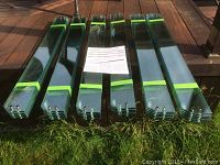 Stacks of multiple clear tempered glass panels with green protective tape on ends laid out on grass