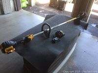 Overview of cordless whipper snipper laid on black mat with battery and charger