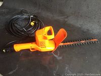Full view of the orange corded hedge trimmer showing the blade, handle, and power cord.