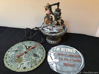 Photo showing the turtle fountain, large outdoor thermometer decorated with butterflies and ferns, and a round retired wall plaque with a figure and text.