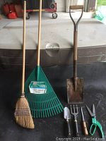 Photo of larger garden tools: natural bristle broom, plastic leaf rake, metal square shovel, small hand tools (dibber, hand rake, small trowel), and green garden shears.