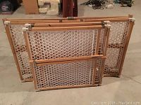 Four wood frame expandable safety gates with white plastic mesh laid upright, showing size differences and design details.