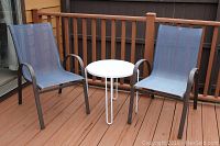 Two outdoor patio chairs with blue mesh seating and one small round white metal table on wood deck.