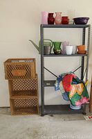 Photo showing metal shelving unit with various items not included and three stacked brown plastic milk crates beside it