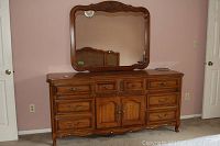 Full view of wooden dresser with attached mirror and carved details, showing shape and style of dresser and mirror.