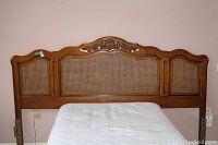 Full view of king size wooden headboard with cane panels and carved floral and shell design at top center.
