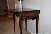 Drop side table shown from an angle emphasizing top surface and single drawer.