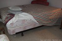 Queen size bed with mattress and box spring on a black metal frame with rolling casters visible under the bed.