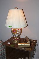Ceramic table lamp with pleated lampshade lit, two brass wall lamps on wooden table.