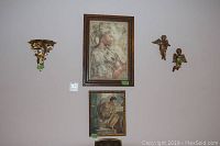 Wall art arrangement showing two framed prints and two small angel figurines mounted on the wall