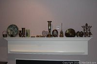 Shelf view showing the entire collection of brass decor items including bowl, door knocker, vases, salt and pepper, candle holders, oil lamp, and pressed flower frames.