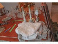 Photo showing three vintage-style table lamp bases with wiring on tabletop with folded lace/crochet tablecloths underneath.