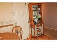 Full view of the Carolyn handpainted wood baker's rack in kitchen setting, showing wood color, door and part of dining table.