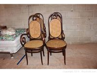 Four wooden cane back chairs with two having arms (captain's chairs), arranged against a basement wall with concrete blocks visible. All chairs have woven cane seats and backs with minor wear.