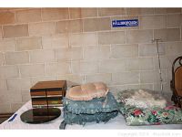 Photo showing stacked seat cushions including floral and green solid cushions, oval pink cushion, and two wooden VHS/cassette storage boxes stacked to the left, and round glass table top on the surface nearby.