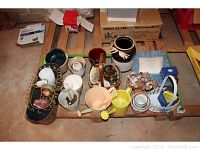 Assorted plant pots and garden items arranged on cardboard on basement floor, showing variety of pot sizes, materials, and colors.