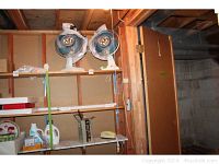 Wide shot of two vintage electric tabletop fans on a wooden shelf, with a rotary dial phone, shelf brackets, cleaning product, and light bulbs visible on lower shelves