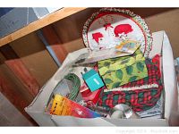 Box with assorted recycled bows, green wire, red and black plaid fabric, and Christmas plate cover.