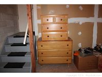 Two piece wooden dresser set stacked together in basement area near stairs, showing full view of both dressers