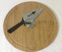 Photo of pizza cutter placed on bamboo pizza board, showing Nuwave branding on blade cover and black handle.
