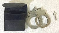 Handcuffs, key, and black carrying case laid flat on white towel background.