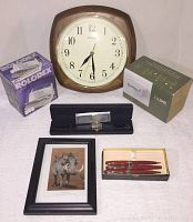 Photo showing Seiko wall clock, Rolodex box, EZLoad box, wristwatch in black case, framed rhino print, and boxed set of pens.