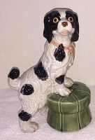 Side angle view of the ceramic King Charles spaniel on green stool figurine showing the detailed black and white coloring and pink ribbon.