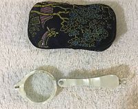 Lorgnette glasses and original fabric case on textured background.