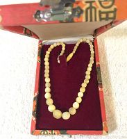 Full view of vintage stone bead necklace laid inside decorative box with burgundy velvet lining.