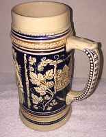 Side view of vintage ceramic beer stein showing detailed relief scene with figures and decorative handle.