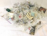 Wide-angle image showing numerous small plastic bags containing various costume jewelry pieces spread out on a white surface.