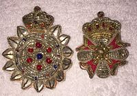 Front view of two embroidered fabric brooches with heraldic motifs, one circular with scalloped edge and one shield-shaped with red fabric and bead details