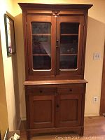 Front view of two-piece wooden china cabinet with glass doors on top and wooden doors on bottom, showing natural wood finish and original hardware.