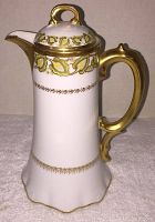 Side view of the chocolate pot showing porcelain body with gold and green leaf decoration and gold handle.