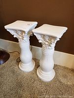 Photo front view of two white concrete pedestals side by side on carpeted floor, showing overall design and scale