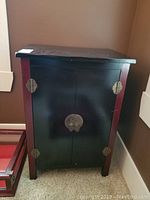 Front view of the wooden oriental-style cabinet showing its black body with reddish wood accents and metal lock hardware.