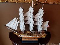 Full front view of detailed model sailboat with white sails and wooden base
