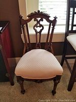 Full view of the vintage hand-carved occasional chair showing the upholstered seat and carved wood frame with turned legs and casters.