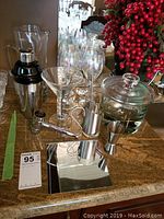 Full view of bar items arranged on countertop including cocktail shaker, martini glasses, wine glasses, ice bucket, strainer and accessories.