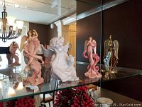 Glass shelf displaying five angel figurines and decorations in various styles and colors.
